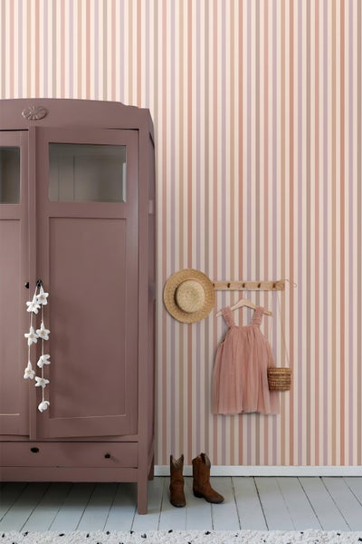 Gestreifte Tapete in Pastelltönen in einem Kinderzimmer neben einem Schrank, einem Kleiderhaken mit Kleid und Hut sowie Stiefeln auf dem Boden.