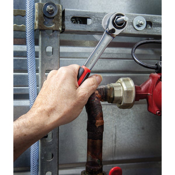 Eine Hand benutzt eine Umschaltknarre von Virax an einer Rohrleitung.