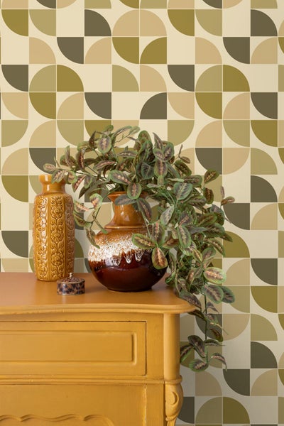 Vliestapete mit retro-geometrischem Muster aus Halbkreisen in Grün- und Brauntönen hinter einer gelben Kommode mit Vasen und Zimmerpflanze.