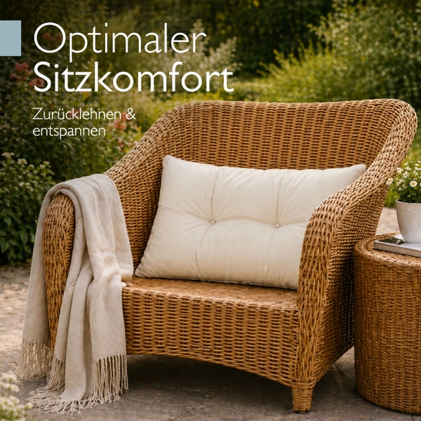 Gartensessel aus Rattan mit weichem Sitzpolster und einer hellen Decke auf einer Terrasse im Garten.