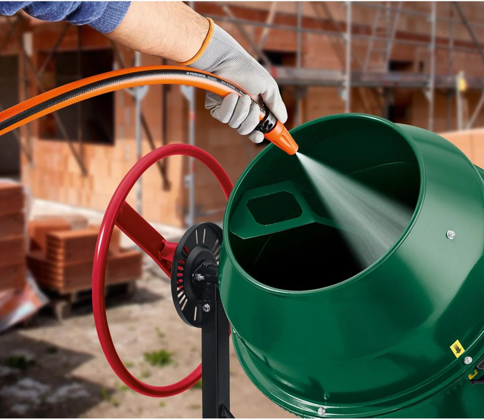 Reinigung der Trommel einer Betonmischmaschine mit einem Wasserstrahl aus einem Gartenschlauch auf einer Baustelle.