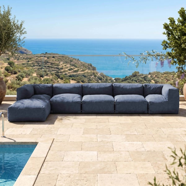 Modernes modulares Outdoor-Sofa in Blau auf einer hellen Terrasse mit Natursteinfliesen, Pool und weitem Meerblick.