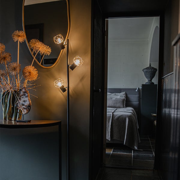 Dekoratives Interieur mit Stehlampe, Spiegel und Blick in ein Schlafzimmer.