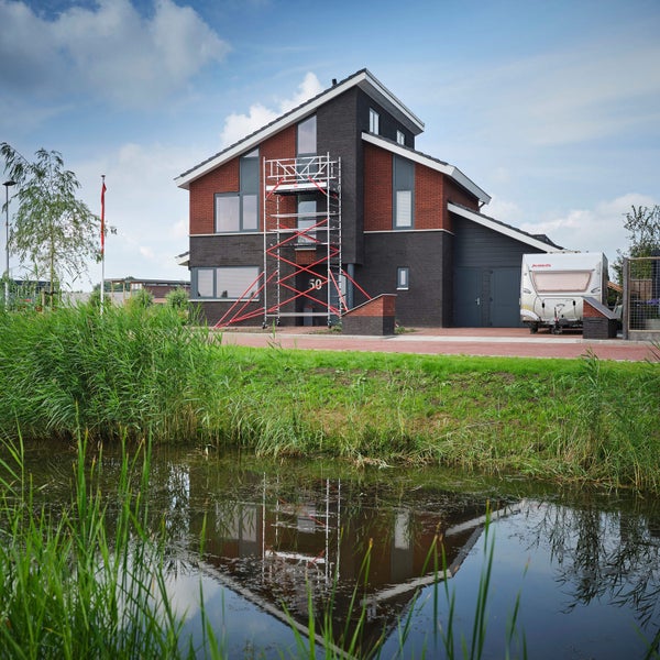 Ein zweistöckiges Wohnhaus mit Gerüst neben einem Teich.