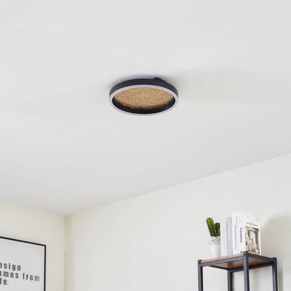 Runde Deckenleuchte mit schwarzem Rahmen und goldfarbener strukturierter Innenfläche in einem hellen, modern eingerichteten Raum.