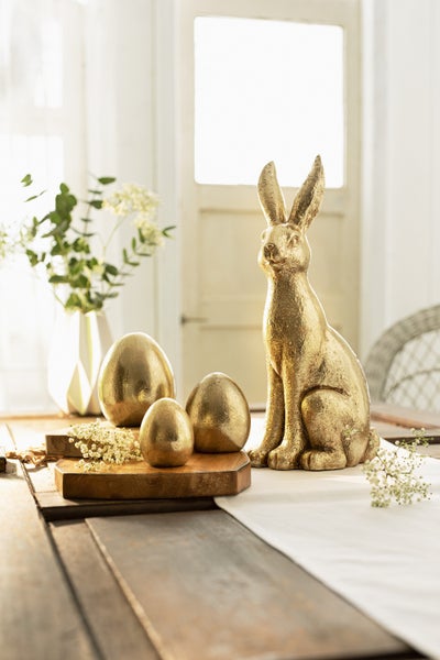 Dekoration mit goldenem Osterhasen und Ostereiern auf einem Tisch.