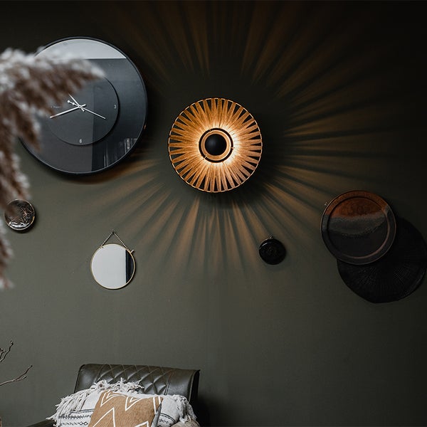 Dekorative Wandleuchte mit Lamellendesign und strahlenförmigem Lichteffekt an einer Wand mit runden Dekorationsobjekten.