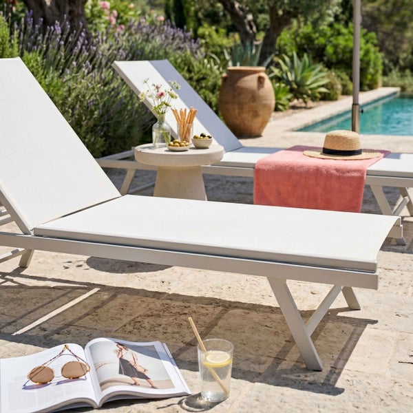 Zwei weiße Gartenliegen auf einer Terrasse am Pool mit Beistelltisch, Magazin und Dekoration.