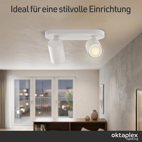 Moderner weißer Deckenstrahler zwei-flammig mit zylindrischen Lampenköpfen in einem hellen Wohnzimmer, oktaplex lighting Logo.