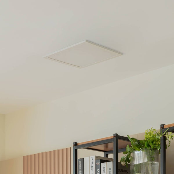Quadratisches LED-Panel an einer Decke in einem hellen, organisierten Raum über einem Regal mit Büchern und einer Pflanze.