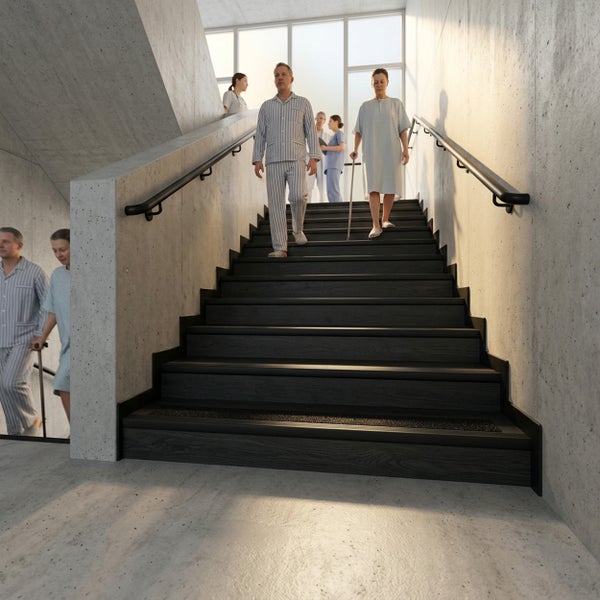 Modernes Treppenhaus mit dunklen Treppenstufen in Holzoptik, schwarzen Sicherheitskanten, Handläufen und Sichtbetonwänden.