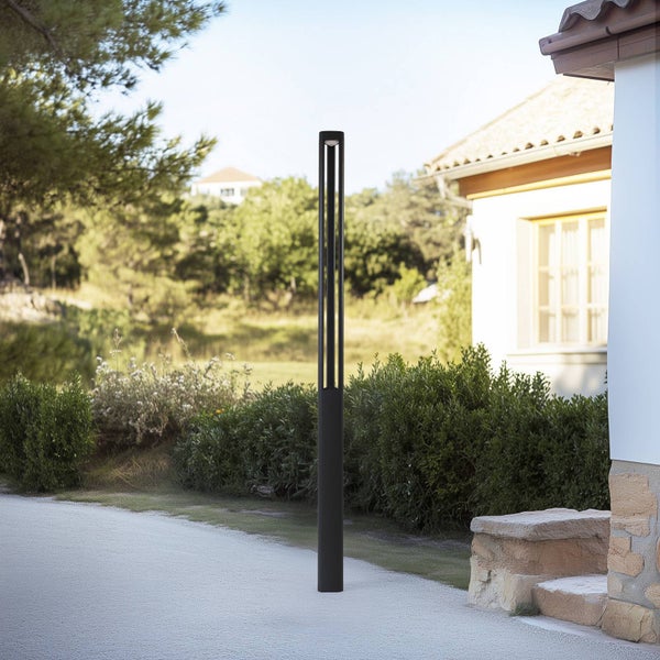 Moderne, schwarze Wegeleuchte in einem Garten neben einem Kiesweg und grünen Sträuchern.