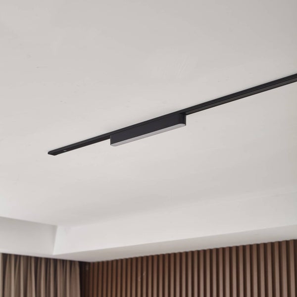 Modernes schwarzes Schienensystem mit einem linearen LED-Modul an einer weißen Zimmerdecke über einer Wand mit Holzpaneelen.