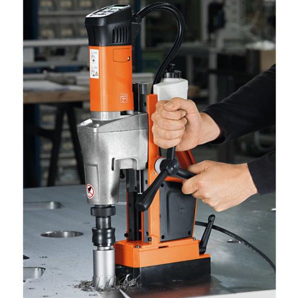 Magnet-Kernbohrmaschine bei der Arbeit auf einer Metallplatte mit Metallspänen, bedient durch zwei Hände an den Hebeln.