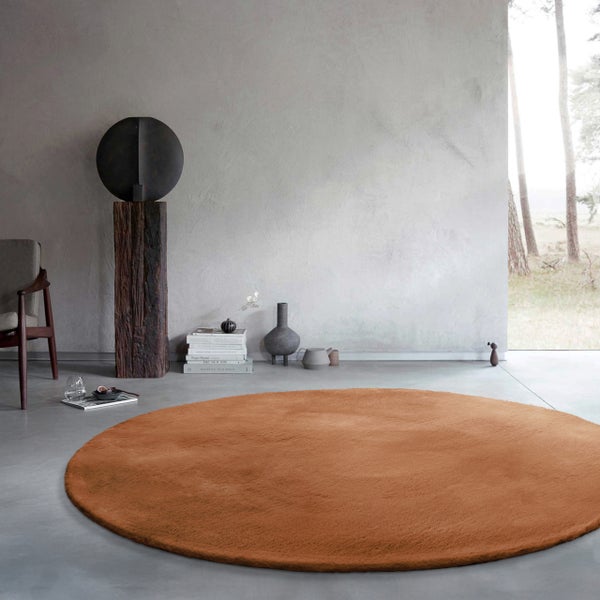 Runder, flauschiger Teppich in Orange-Braun in einem modernen Wohnzimmer mit Betonboden, grauen Wänden und minimalistischer Einrichtung.