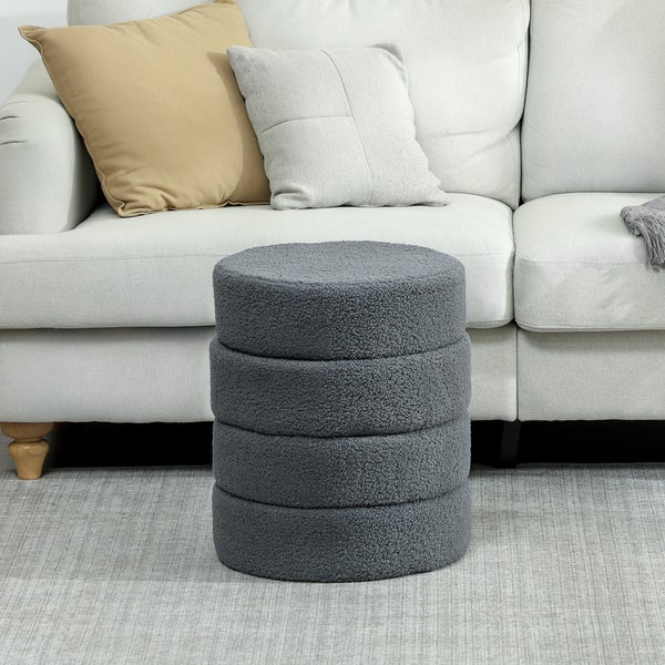 Grauer, runder Hocker vor einem Sofa