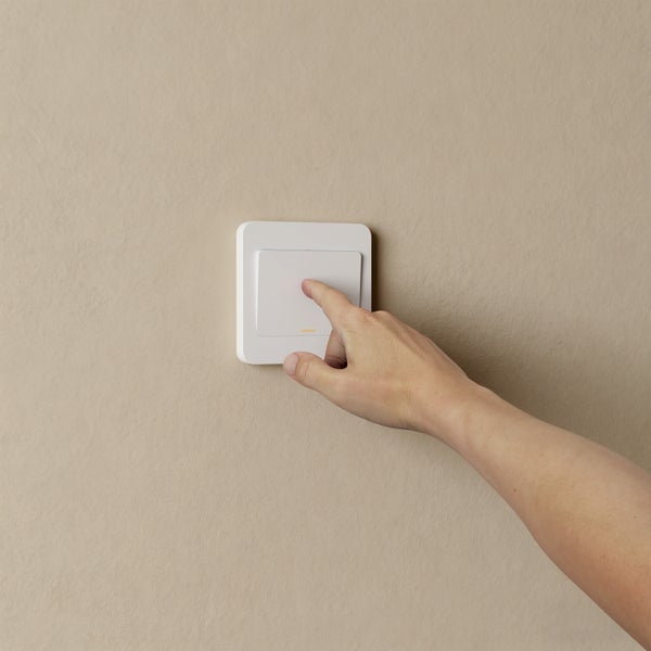 Hand betätigt einen flachen weißen Lichtschalter an einer Wand.