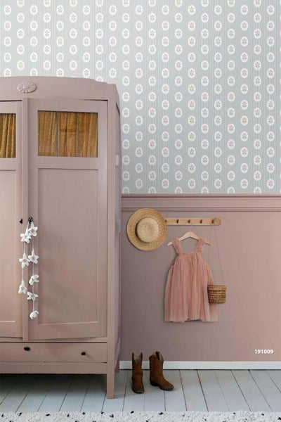 Vintage-Zimmer mit rosa Kleiderschrank, gemusterter Tapete und Wandpaneelen. An einer Hakenleiste hängen Hut und Kinderkleid.