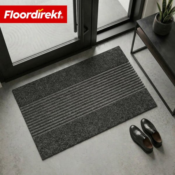 Floordirekt Schmutzfangmatte in Anthrazit mit Streifenmuster im modernen Eingangsbereich vor einer Glastür neben schwarzen Schuhen.