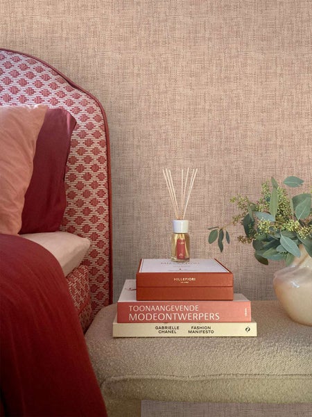 Strukturierte Tapete in einem Schlafzimmer mit einem gepolsterten Bettgestell und einem Stapel Bücher mit einem Duftdiffusor auf einem Hocker
