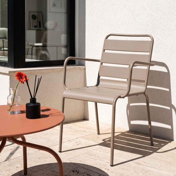 Moderner Gartenstuhl aus Metall mit Armlehnen und Latten-Design neben einem runden Beistelltisch auf einer sonnigen Terrasse.