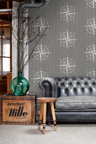 Wohnszene mit Sofa, Hocker, Holzkiste und Tapete mit Kompassmuster
