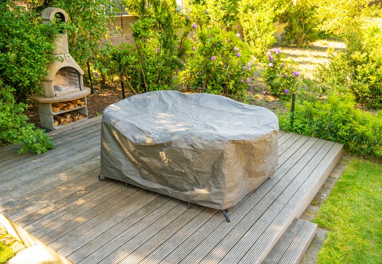 Gartenszene mit Terrassenofen, Holzstapel und abgedeckter Sitzgruppe im Freien