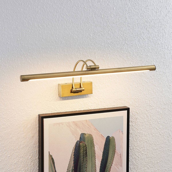 LED Bilderleuchte aus mattem Messing, montiert über einem gerahmten Bild auf einer hellen, strukturierten Wand.