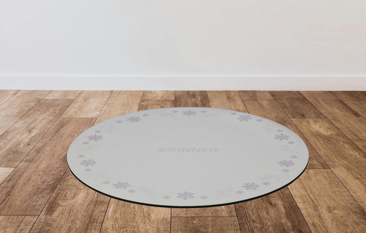 Runde, graue Krinner Weihnachtsbaumständer-Unterlage mit Schneeflocken-Muster auf einem Holzboden.