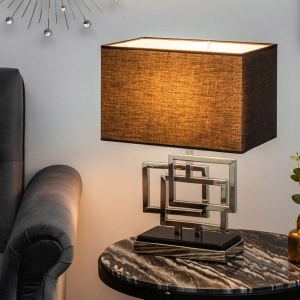 Dekorative Tischleuchte mit rechteckigem Schirm und silberfarbenem, geometrischem Gestell auf einem runden Tisch
