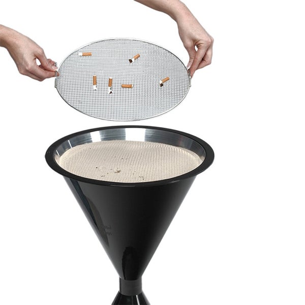 Zwei Hände heben ein rundes Metallsieb mit Zigarettenstummeln aus einem schwarzen Standaschenbecher mit Sand.