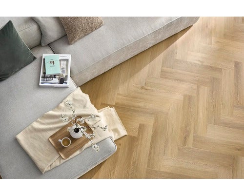 Ansicht eines Wohnzimmers mit einem hellen Sofa und einem Fischgrät-Parkettboden