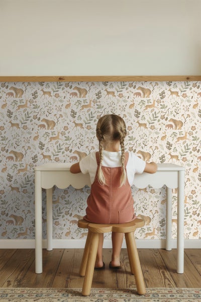 Mädchen sitzt an weißem Schreibtisch vor einer Tapete mit Tiermotiven