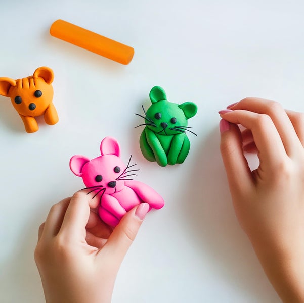Hände modellieren kleine Tierfiguren wie Mäuse aus bunter Knete.
