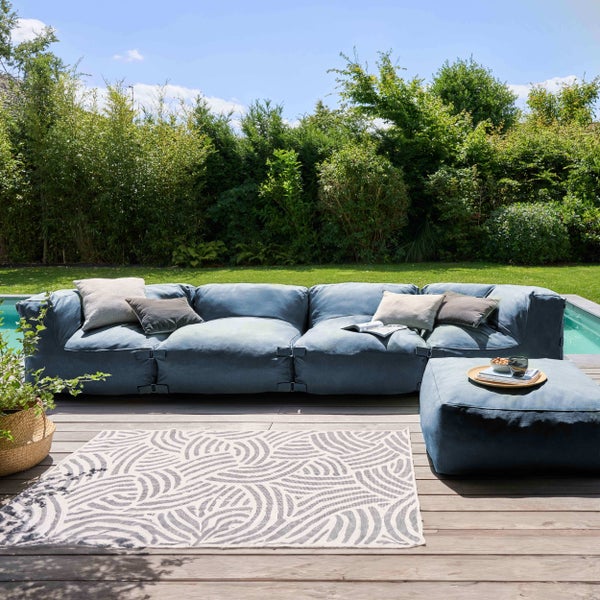 Modulares Garten-Lounge-Sofa mit passendem Hocker und Outdoor-Teppich auf einer Holzterrasse neben einem Pool im Garten.