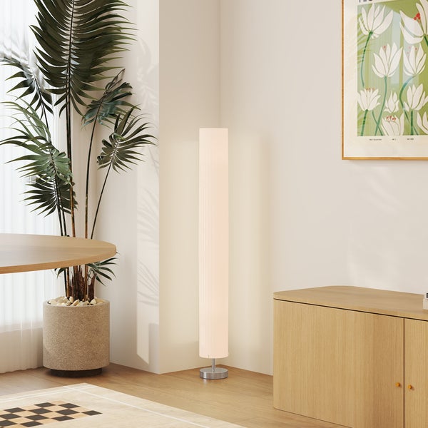 Moderne zylindrische Stehleuchte in einer hellen Zimmerecke neben einer großen Pflanze und einem Sideboard aus Holz.
