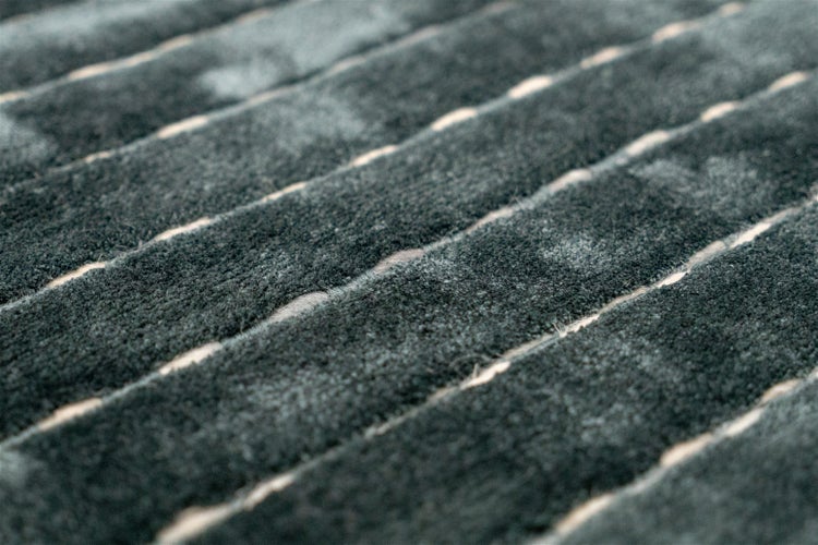 Detailaufnahme eines weichen Teppichs mit einer gerippten Oberflächenstruktur und hellen Linien.