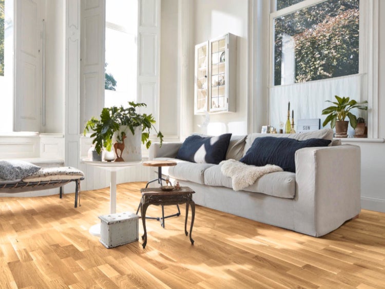 Helles Wohnzimmer mit Parkettboden aus Eiche, einem Sofa mit dunklen Kissen und großen Fenstern.
