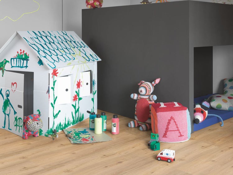 Helles Kinderzimmer mit selbstbemaltem Spielhaus aus Pappe, Holzfußboden, Stofftieren und Malfarben.