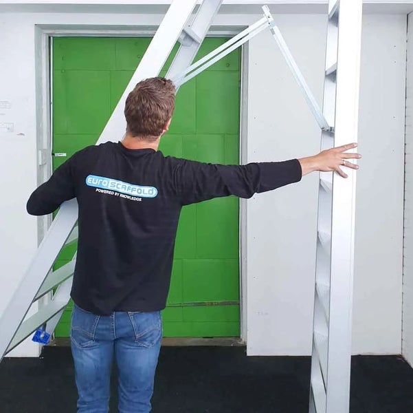 Mann trägt eine Aluminiumtreppe vor einer Tür