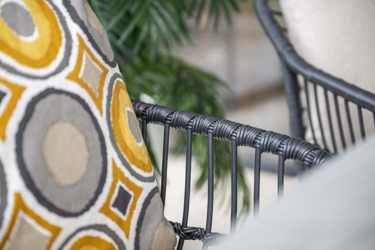 Detailansicht eines Gartenstuhls mit dunklem Kunststoffgeflecht und einem Zierkissen mit geometrischem Muster.