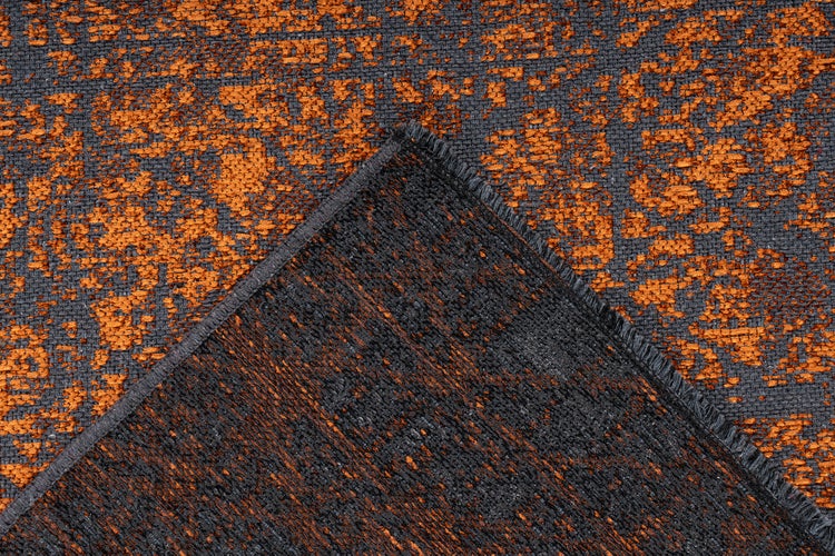 Nahaufnahme eines gewebten Teppichs in Orange und Dunkelgrau mit Vintage-Muster, zeigt die Oberflächenstruktur und eine umgeschlagene Ecke.