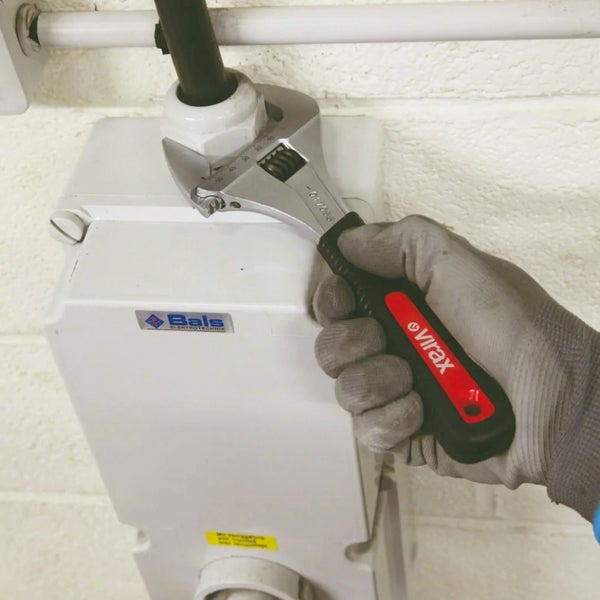 Eine Hand mit Arbeitshandschuh bedient einen verstellbaren Schraubenschlüssel an einem elektrischen Anschlusskasten.