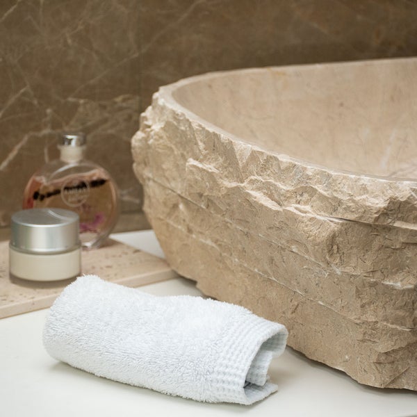 Aufsatzwaschbecken aus Naturstein mit bruchrauer Außenseite und glattem Innenbecken in einer Badezimmerszene.