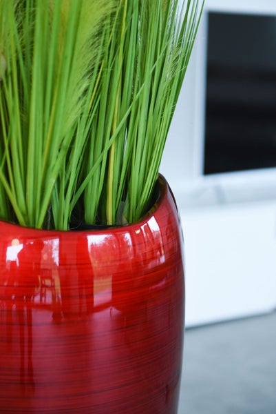 Rote glänzende Vase mit grünem Gras in einer modernen, hellen Wohnumgebung.