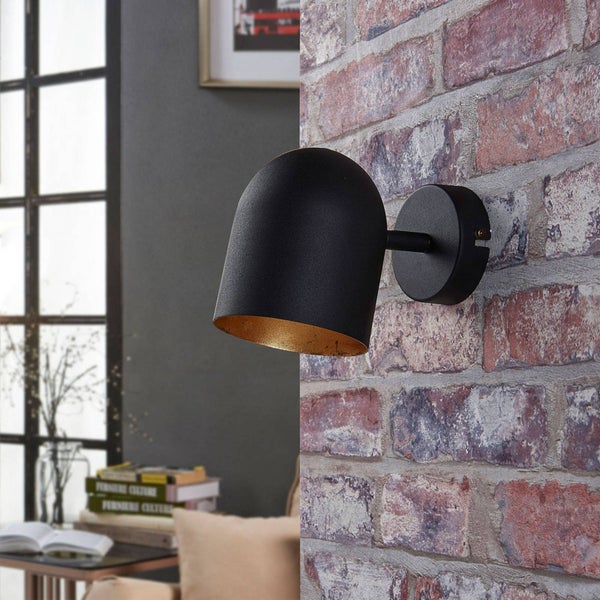 Moderne Wandleuchte aus Metall an einer Ziegelwand. Der Schirm ist außen schwarz und innen goldfarben.