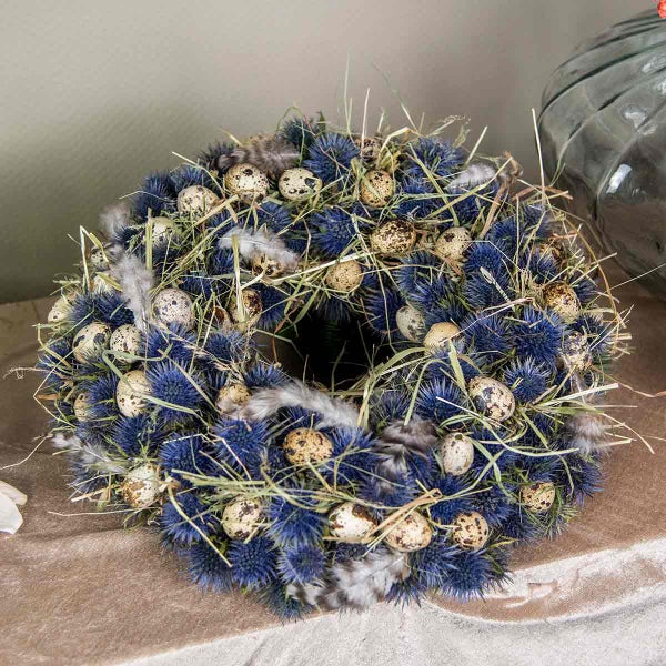 Dekorativer Osterkranz mit Disteln, Wachteleiern, Federn und Stroh