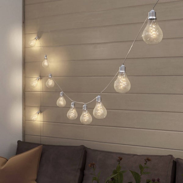 LED Lichterkette mit warmweißen Leuchtmitteln in Glühbirnenform, an einer Holzwand über einem Sofa aufgehängt.