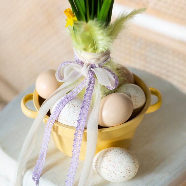 Gelbe Schüssel mit gefärbten Eiern, Narzissen und Schleife als Osterdekoration.