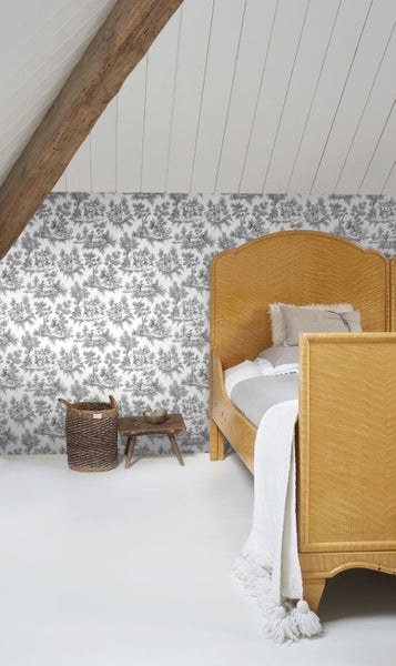 Helles Schlafzimmer mit Toile-de-Jouy-Tapete, Holzbett, Flechtkorb und weißer Holzdecke mit rustikalem Balken.
